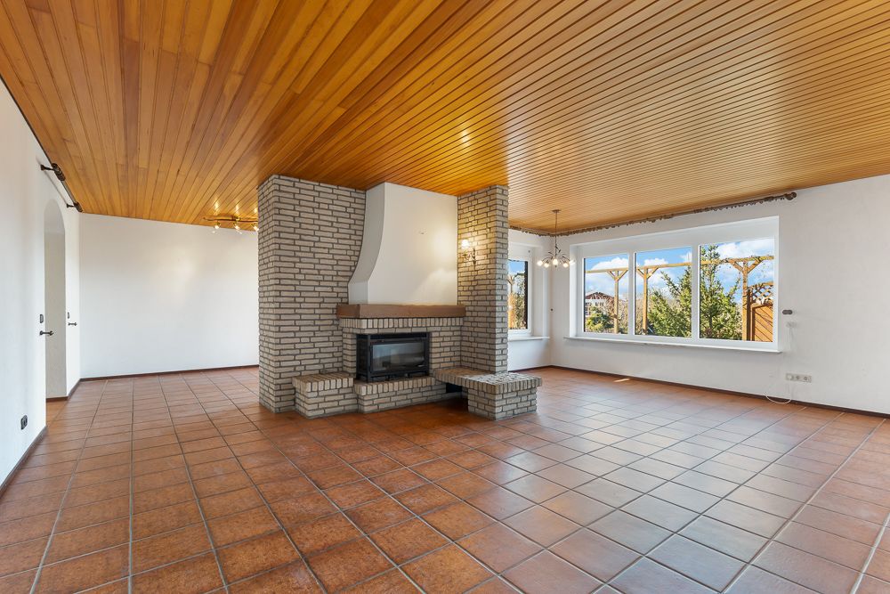 Helles Wohnzimmer mit Kamin, großen Fenstern, Fliesenboden und Holzdecke.