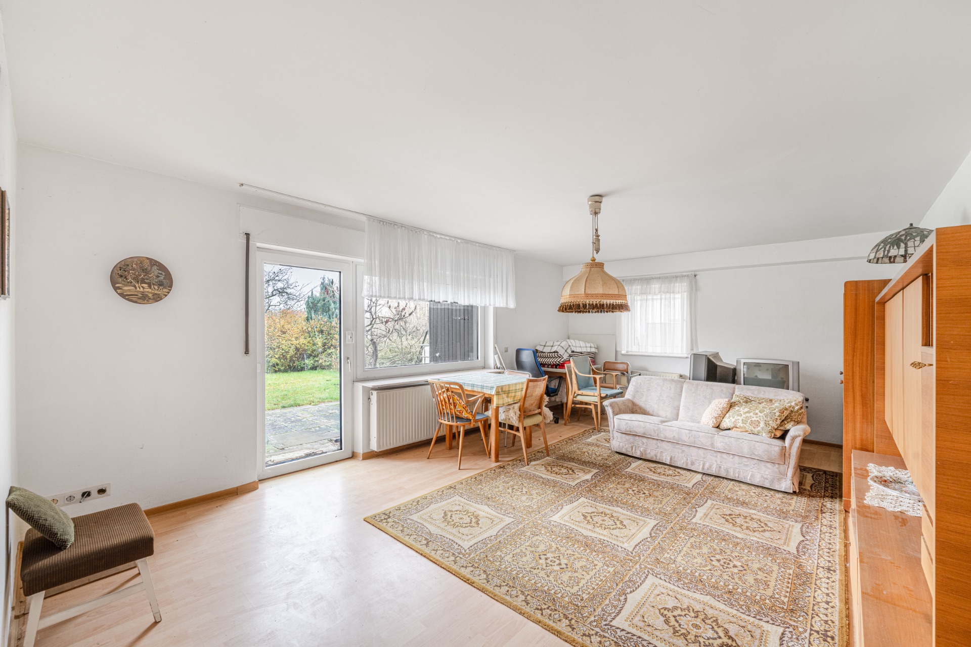 Wohnzimmer mit Teppich, Sofa, Esstisch, Stühlen, TV und Tür zum Garten.