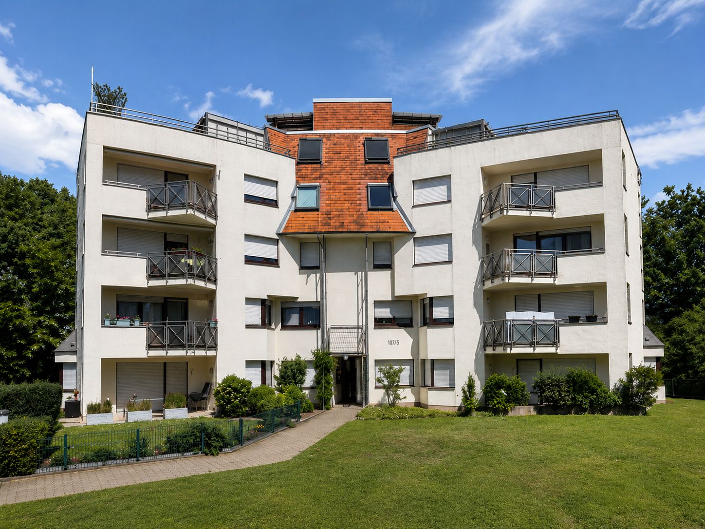 Modernes Wohnhaus mit mehreren Balkonen und großem Vorgarten bei sonnigem Wetter.