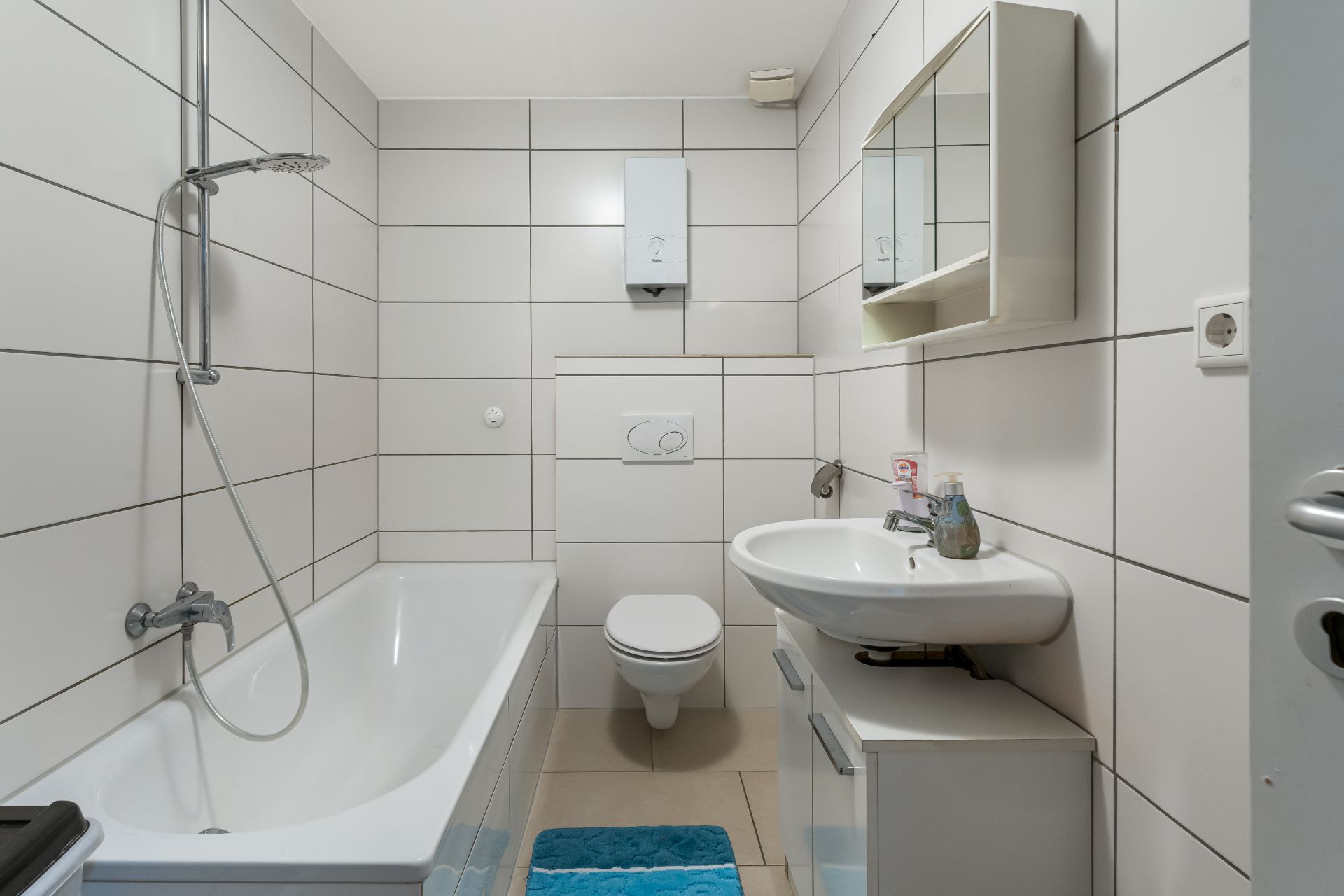 Modernes Badezimmer mit Badewanne, Wandtoilette, Waschbecken und Spiegelschrank.