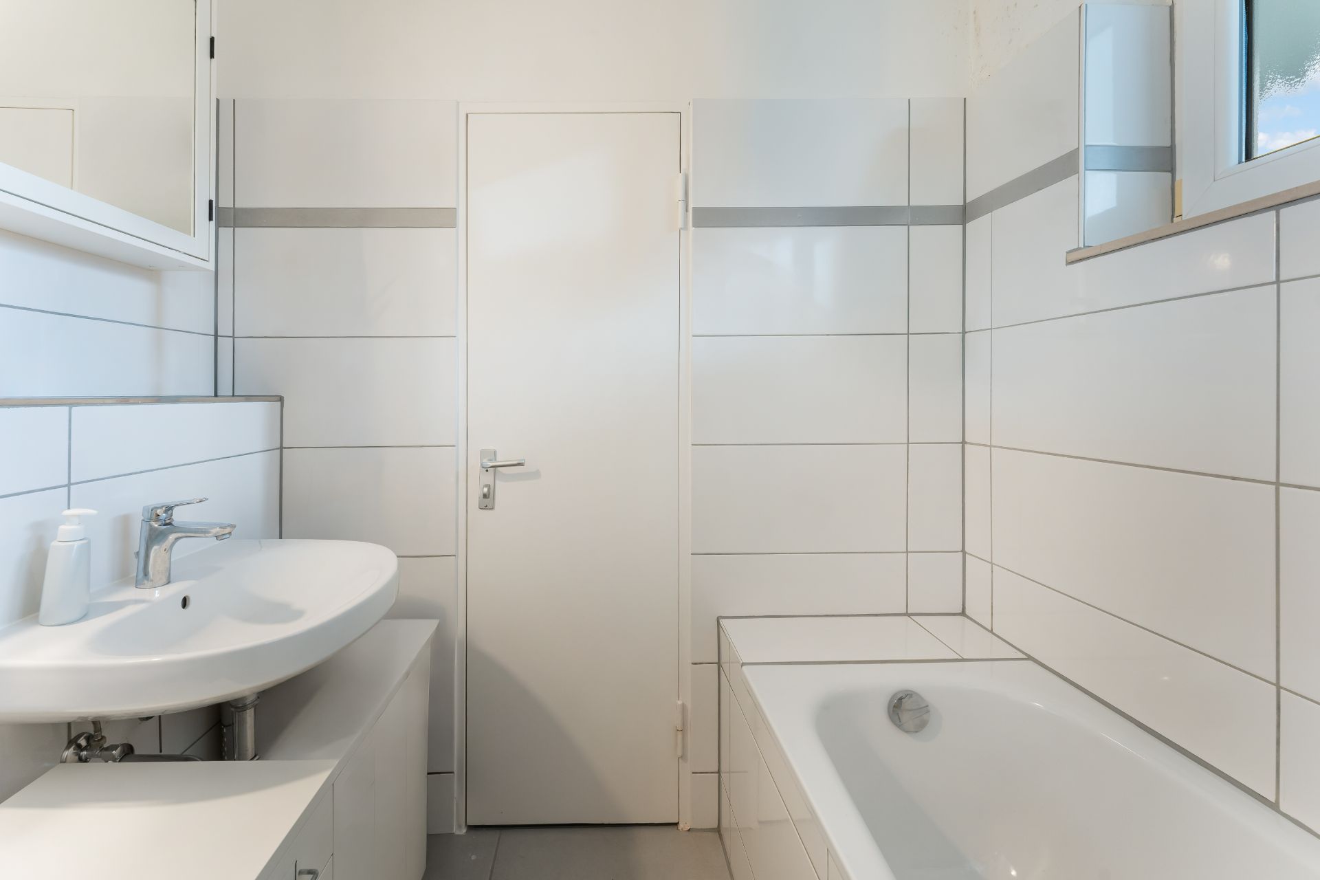 Helles Badezimmer mit Waschbecken, Badewanne und weißen Fliesen.