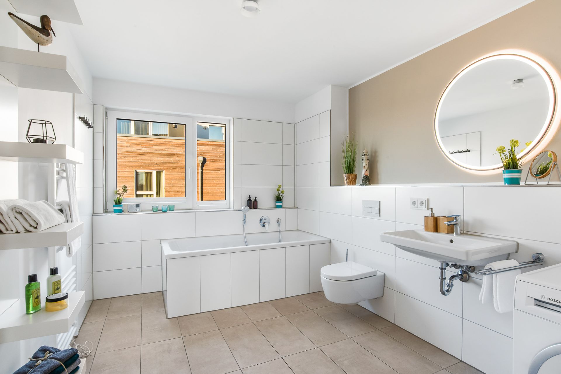 Helles Badezimmer mit Badewanne, WC, großem Spiegel und Waschbecken, Pflanzen und Regalen.