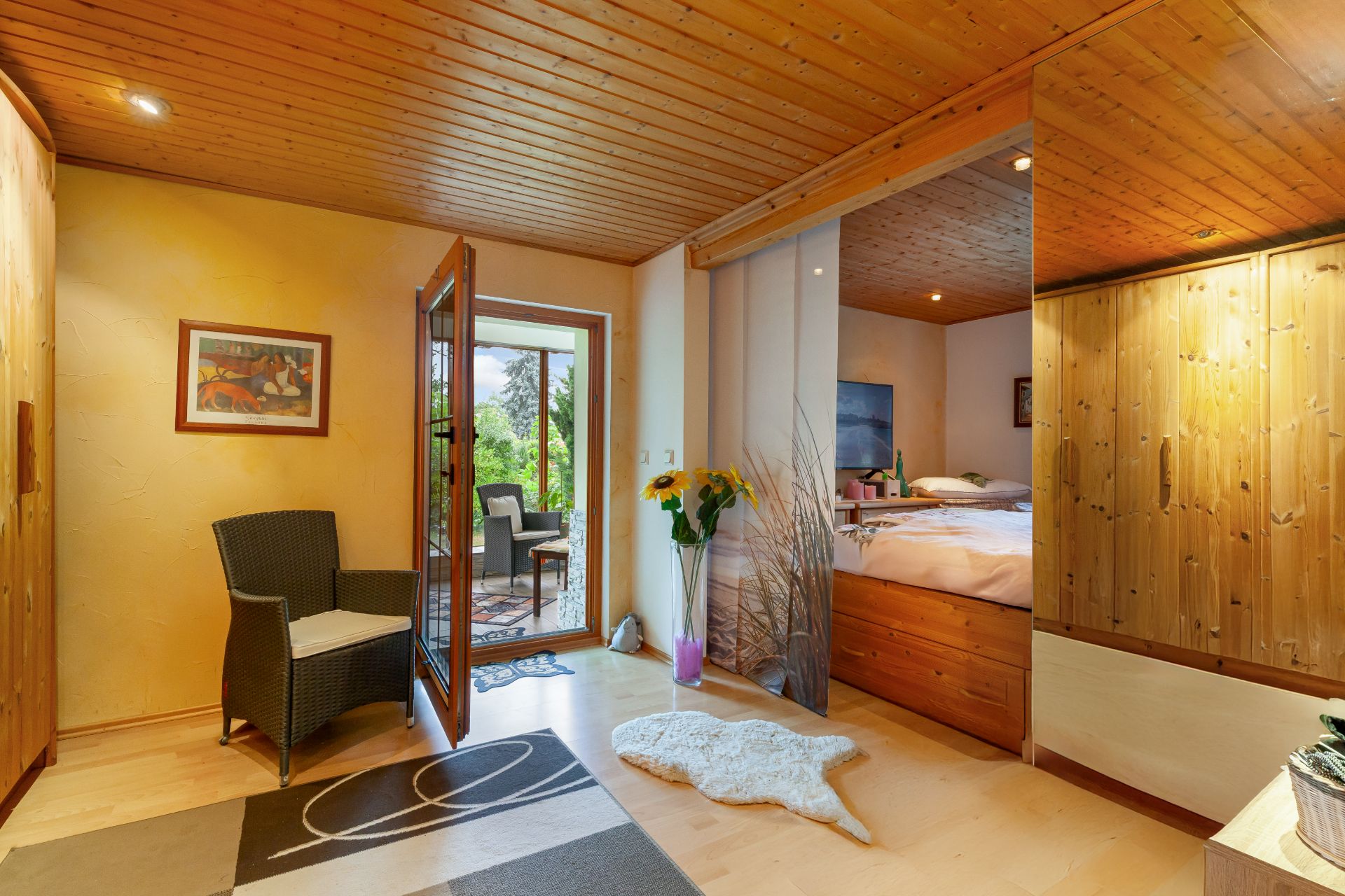 Helles Schlafzimmer mit Holzmöbeln, Sessel, Teppich und Zugang zur Terrasse.