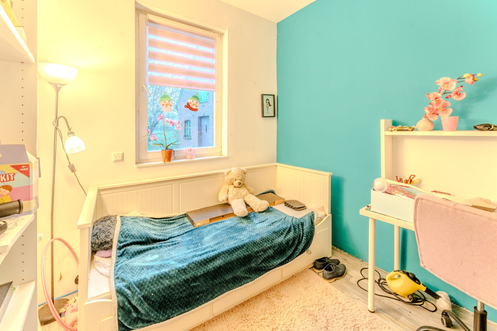 Helles Kinderzimmer mit Einzelbett, Schreibtisch, blauem Wand und Kuscheltier auf dem Bett.