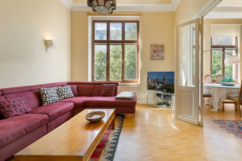 Wohnzimmer mit rotem Ecksofa, Holztisch, großem Fenster und Zugang zum Esszimmer.
