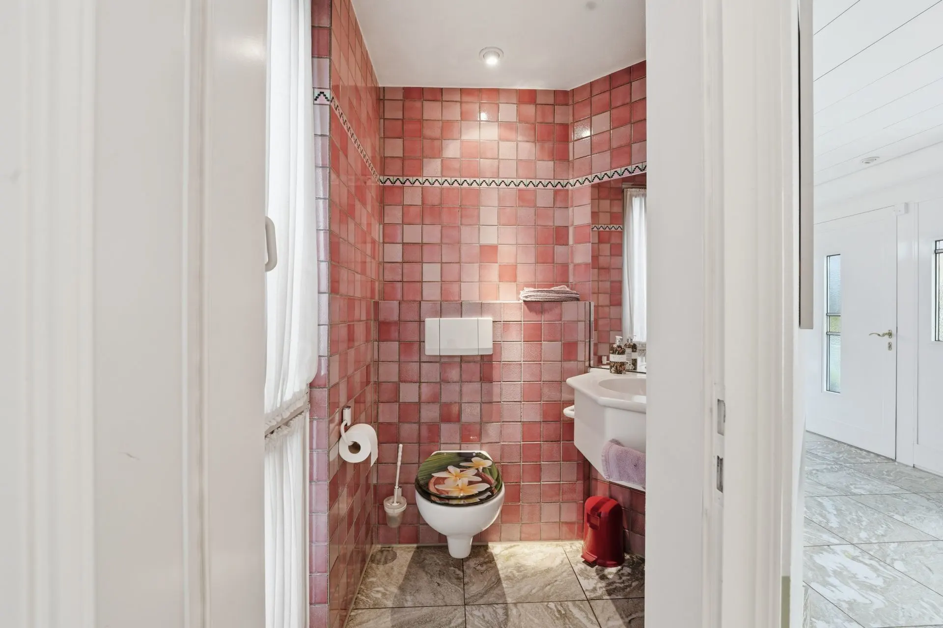 Kleines Bad mit rosa Fliesen, Toilette, Waschbecken und Fenster.