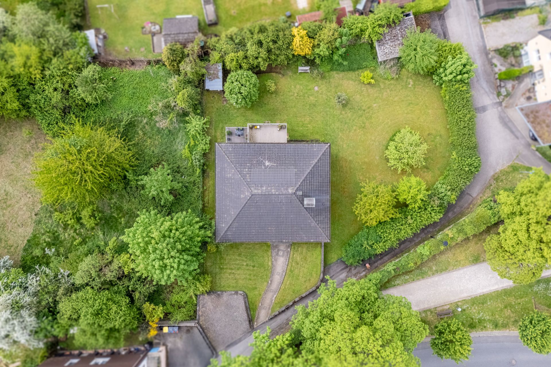 Luftaufnahme eines Einfamilienhauses mit großem Garten, umgeben von Bäumen und Hecken.