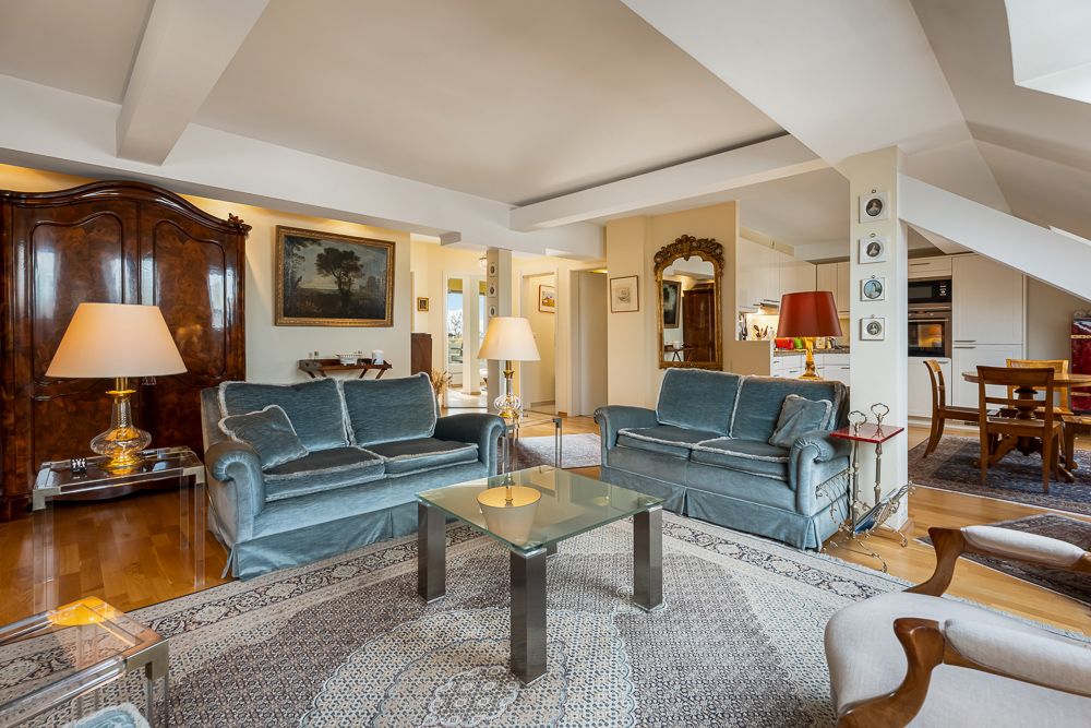 Helles Wohnzimmer mit zwei blauen Sofas, Glastisch, Teppich und Stehlampen.