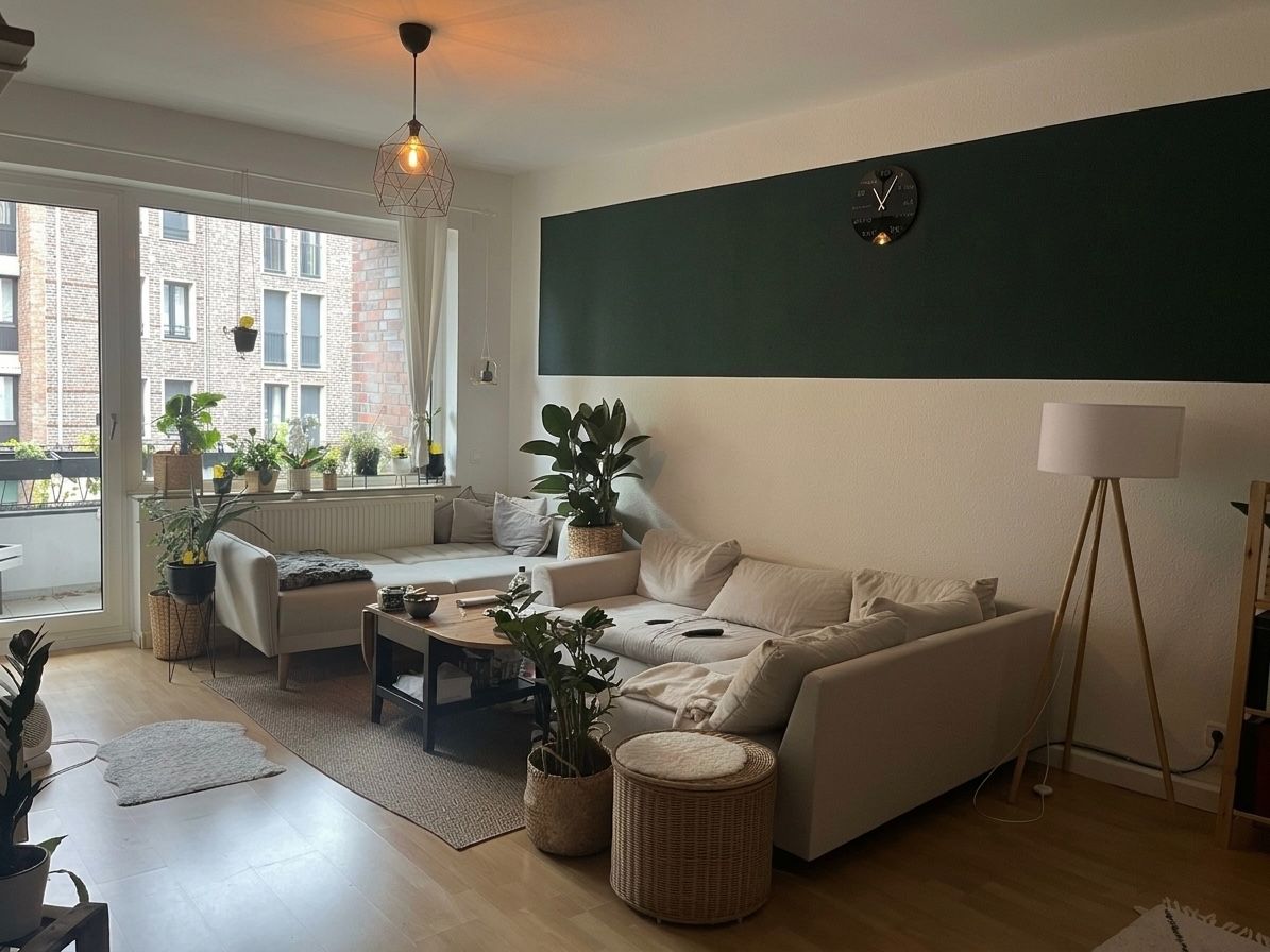 Helles Wohnzimmer mit Ecksofa, Couchtisch, vielen Pflanzen und Stehlampe, große Fenster zur Terrasse.