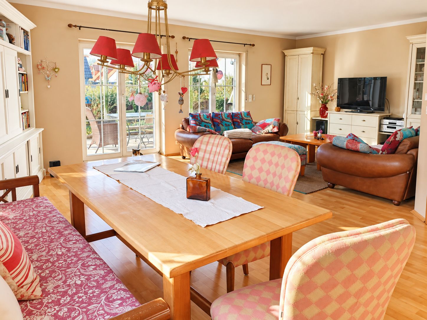 Helles Wohnzimmer mit Esstisch, Polsterstühlen und Sofas, große Fenster mit Blick auf Terrasse.