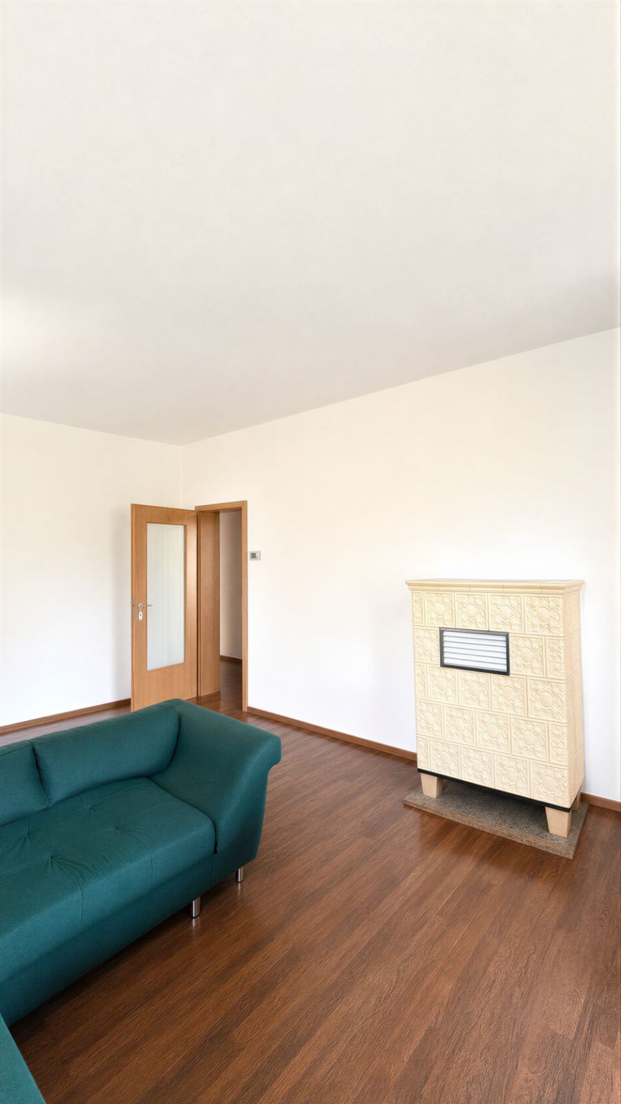 Wohnzimmer mit dunkelgrünem Sofa, Holzboden und hellem Kachelofen.