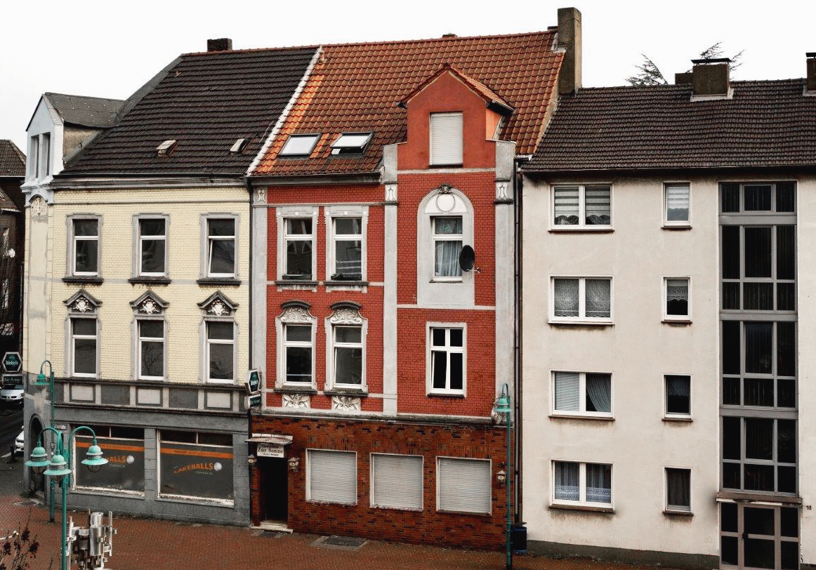 Drei mehrstöckige Wohnhäuser mit unterschiedlichen Fassaden in einer Stadtstraße.