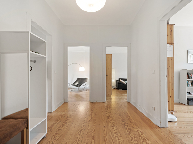 Heller Flur mit Holzboden, drei Türen zu anderen Zimmern, links eine Garderobe mit Spiegel.