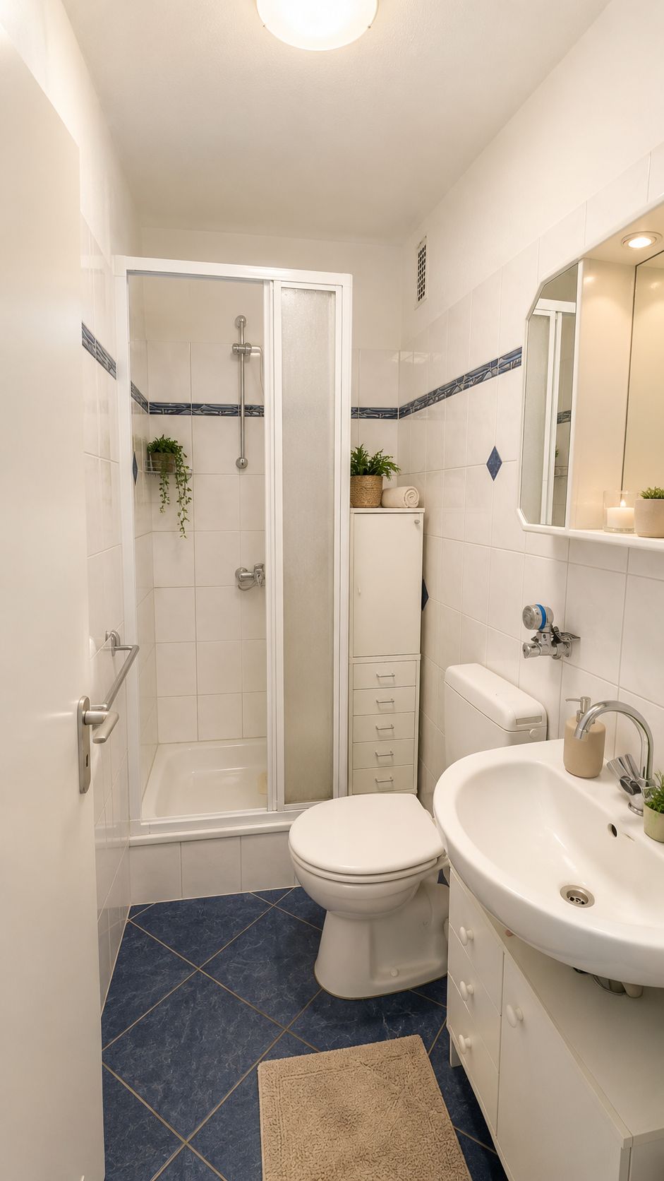 Kleines Badezimmer mit Dusche, WC, Waschbecken, Spiegelschrank und Fliesenboden.