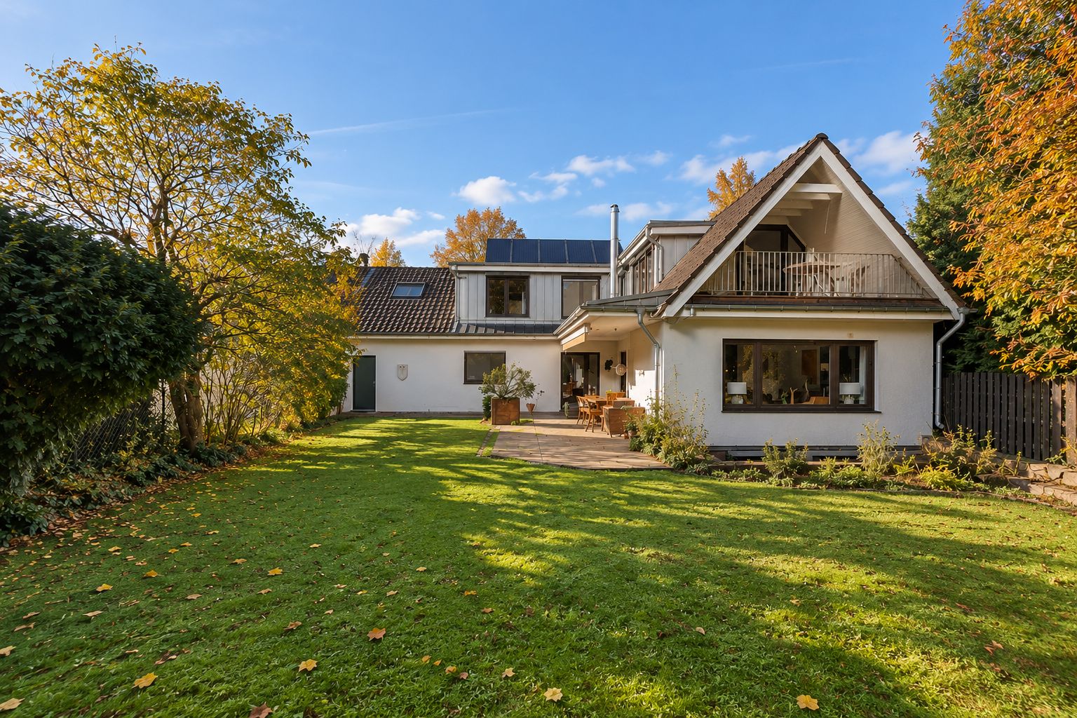 Ein weißes Einfamilienhaus mit Garten, Terrasse und Balkon bei sonnigem Wetter.