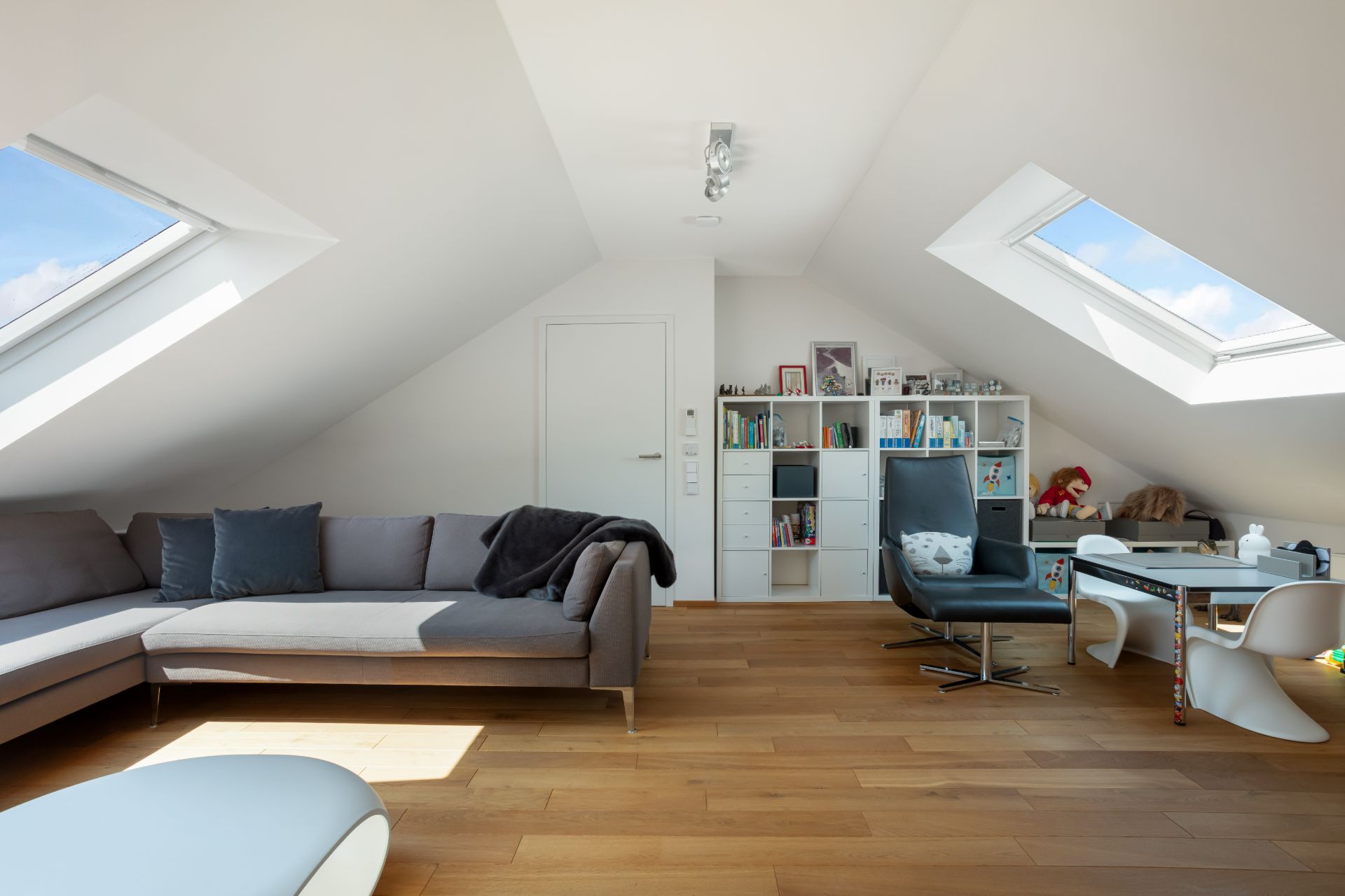 Wohnzimmer im Dachgeschoss mit Ecksofa, Sessel, Regal und Dachfenstern.