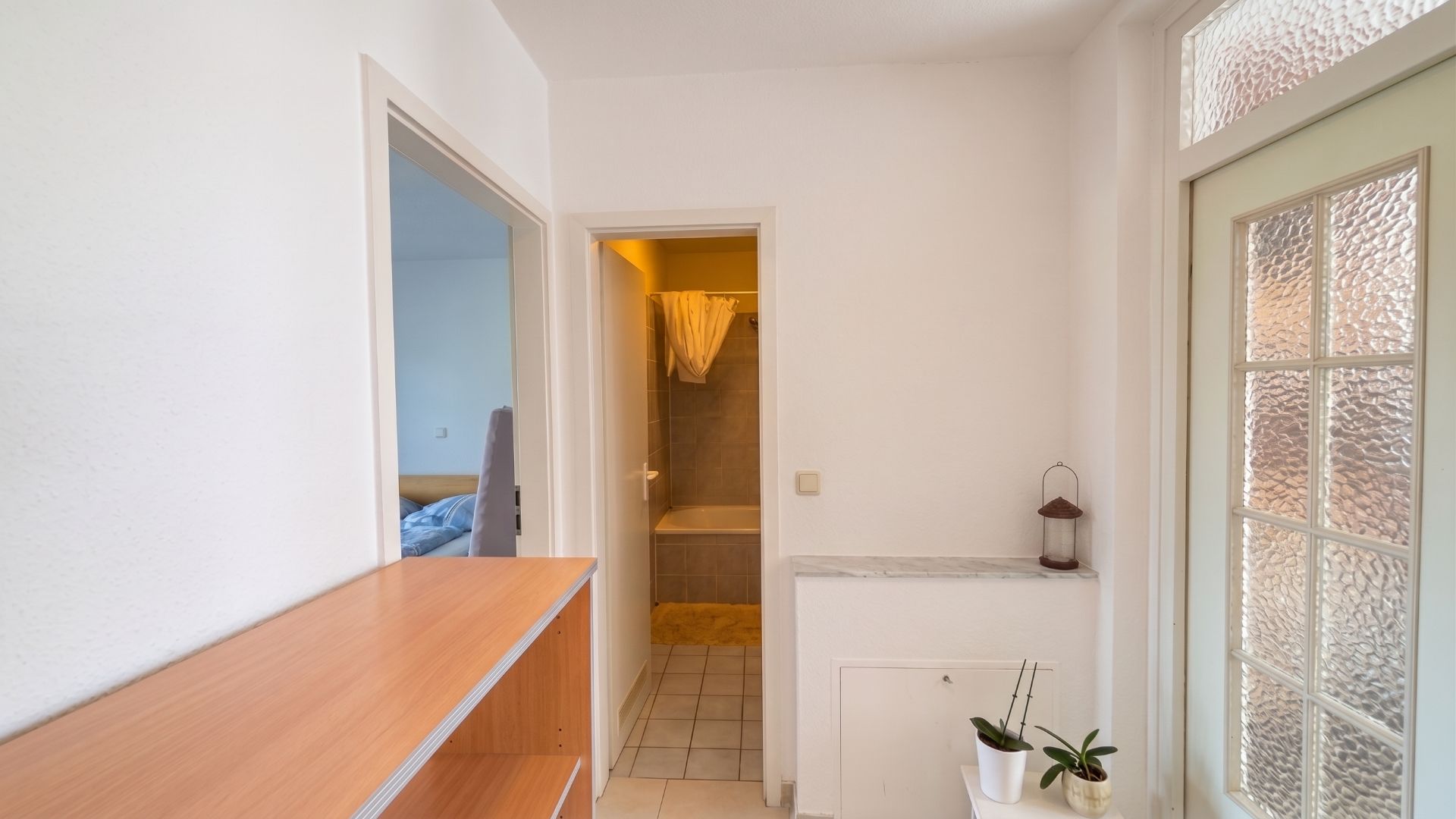 Heller Flur mit Regal, Blick auf Badezimmer und Schlafzimmer, Pflanzen auf einer Ablage.