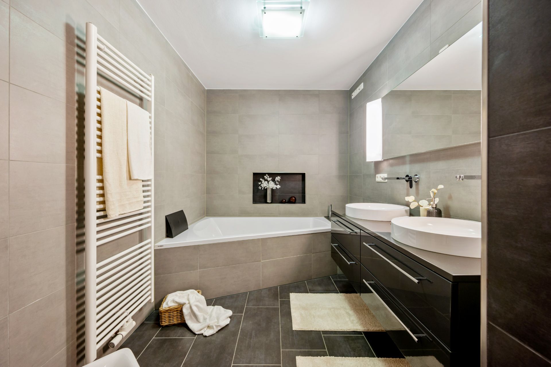 Modernes Badezimmer mit Eckbadewanne, Doppelwaschbecken, Handtuchheizkörper und hellen Fliesen.
