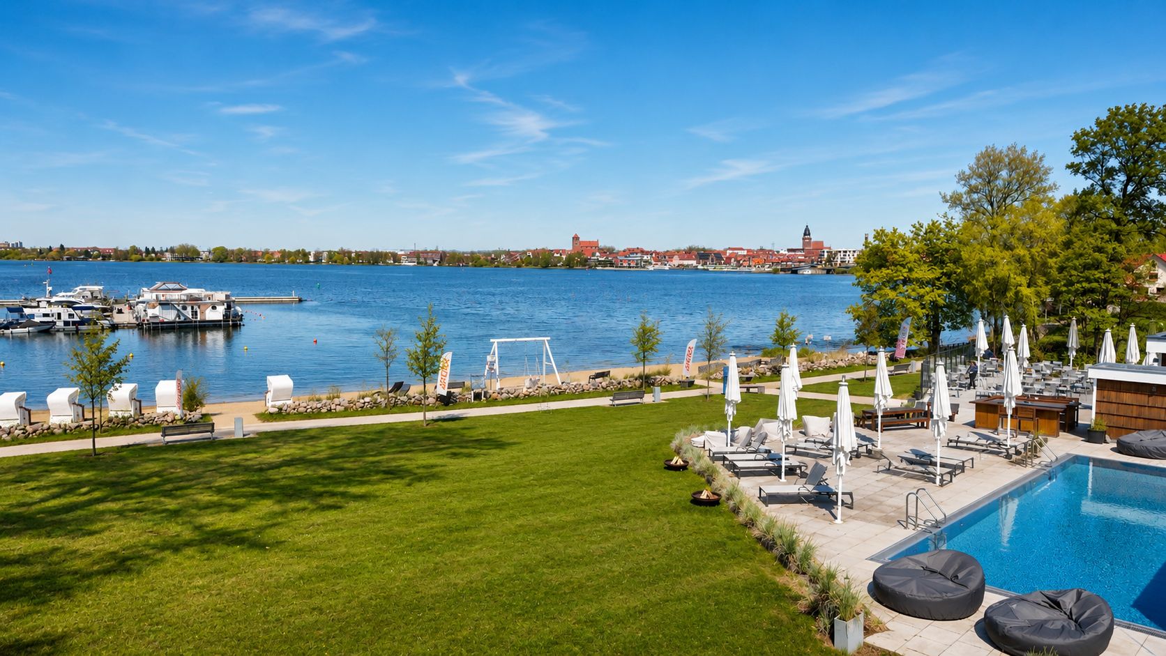 Großer Garten mit Pool, Liegestühlen und Blick auf einen See mit Booten und Stadt im Hintergrund.