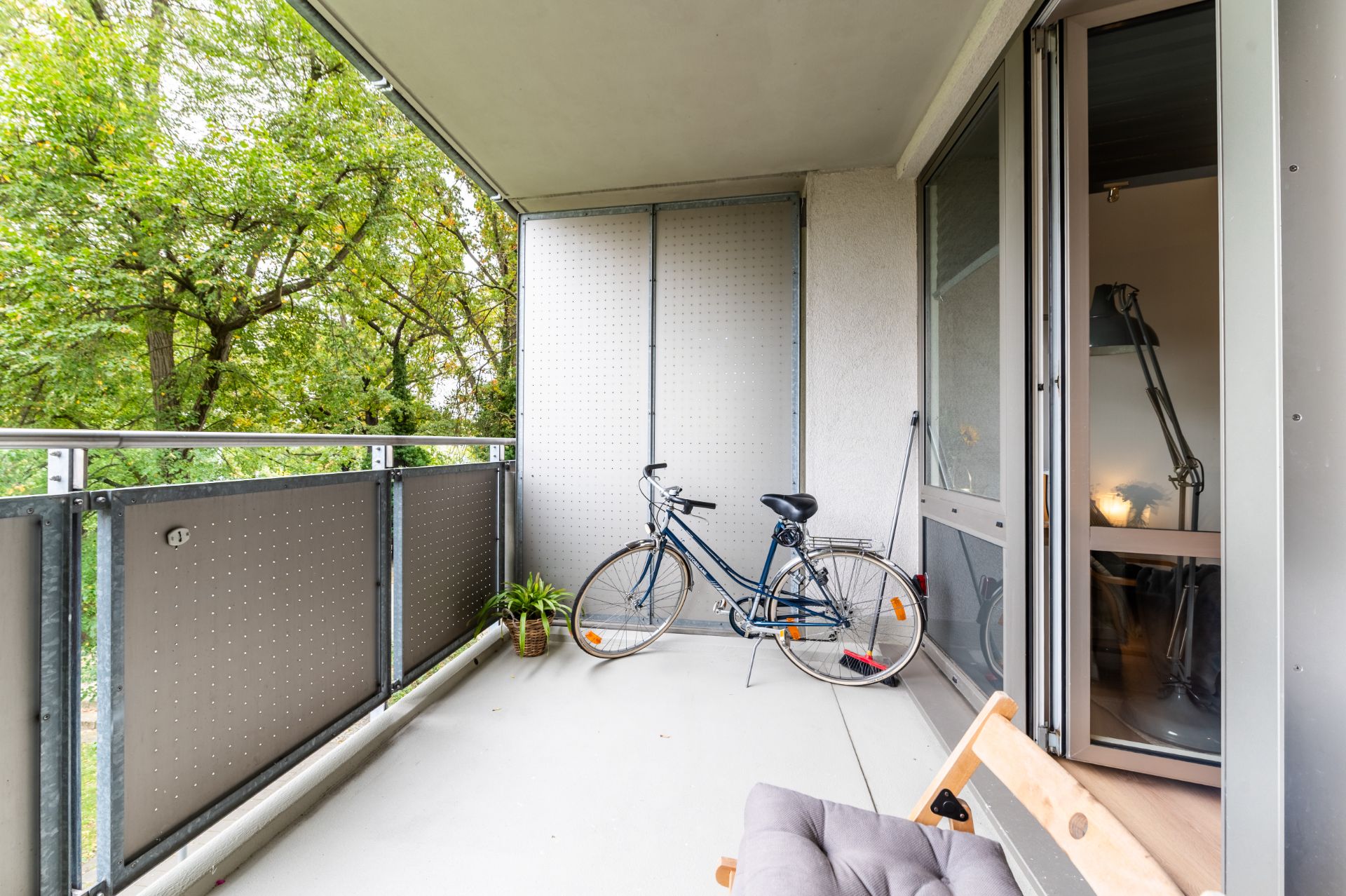Balkon mit Geländer, Fahrrad, Pflanze, Stuhl und Blick auf Bäume.