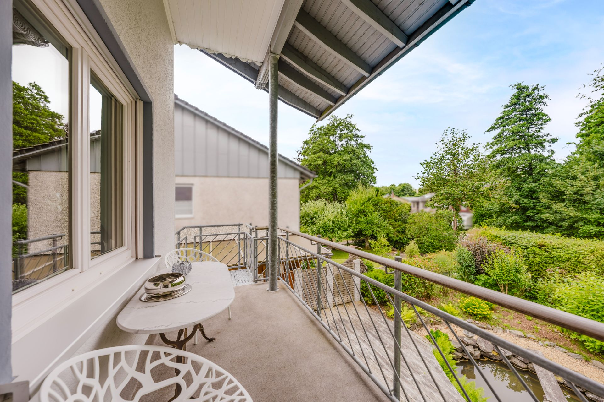 Überdachter Balkon mit kleinem Tisch, zwei Stühlen und Blick auf Garten und Nachbarhaus.