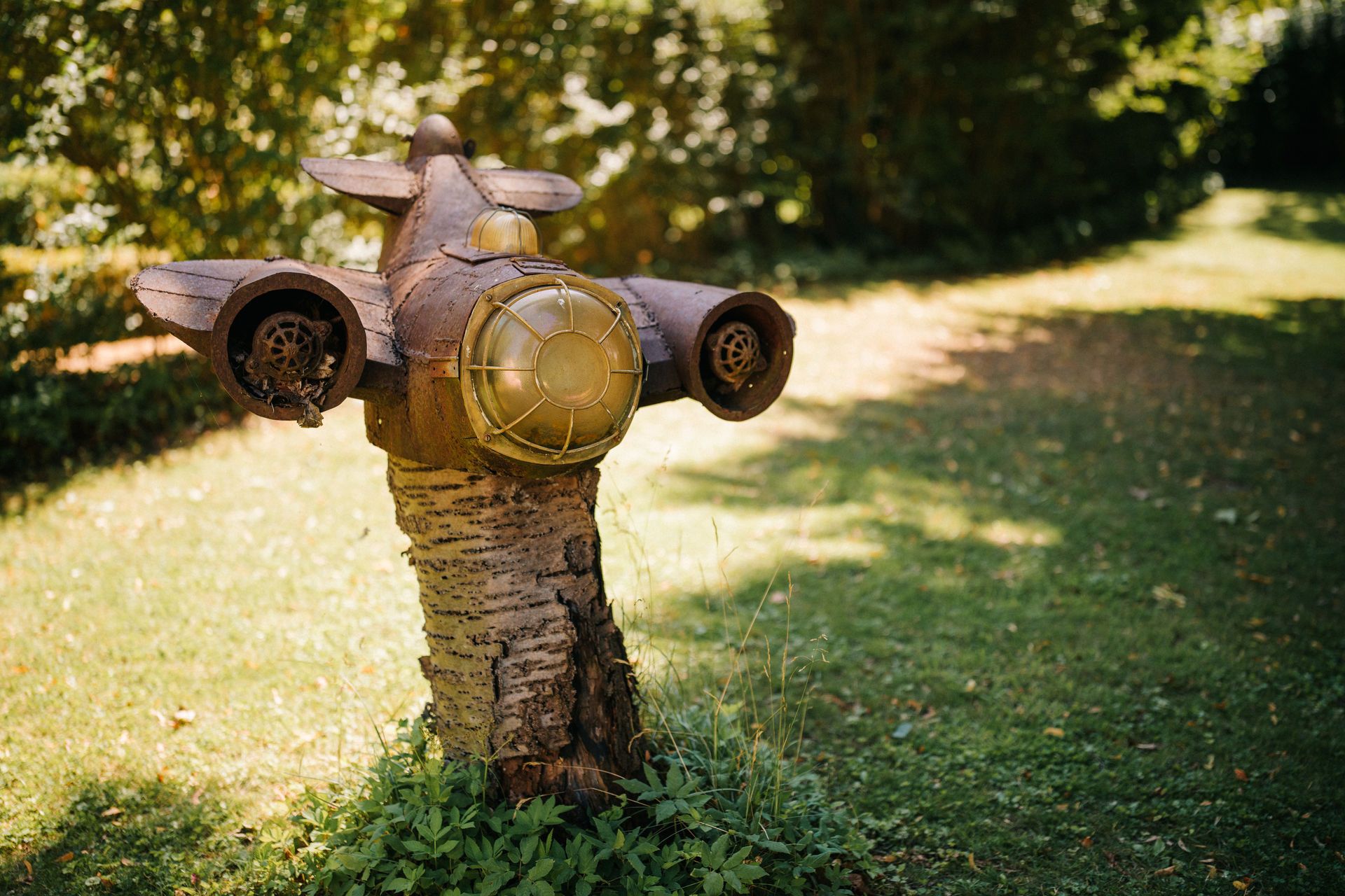 Garten mit einer Skulptur aus Metall auf einem Baumstamm, die ein Flugzeug darstellt.