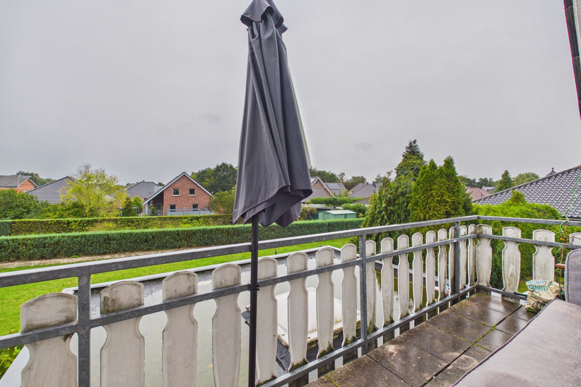 Balkon mit Geländer und geschlossenem Sonnenschirm, Blick auf Garten und Nachbarhäuser.