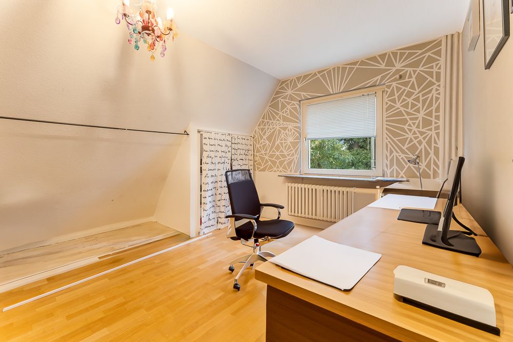 Modernes Arbeitszimmer mit großem Schreibtisch, Bürostuhl, Wanddeko und Fenster mit Blick ins Grüne.