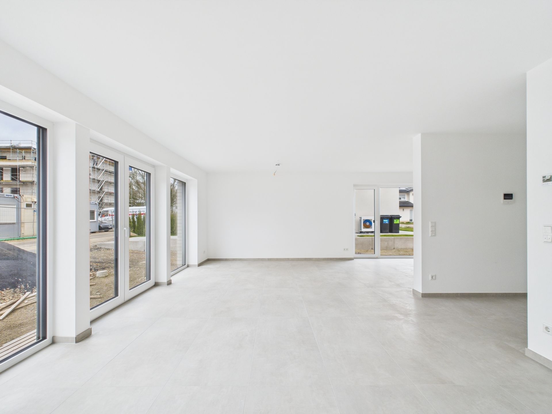 Heller, leerer Raum mit großen Fenstern und Fliesenboden in einem Wohnhaus.