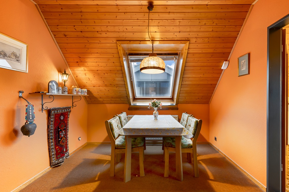 Essbereich mit Holztisch, sechs Stühlen, Fenster im Dach und orangenen Wänden.