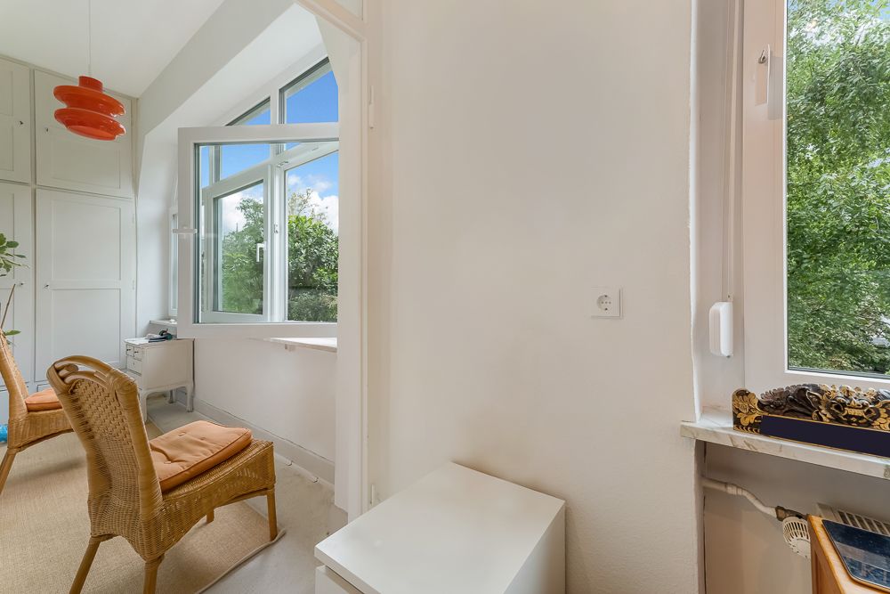 Heller Raum mit großen Fenstern, zwei Korbstühlen und weißem Wandschrank.