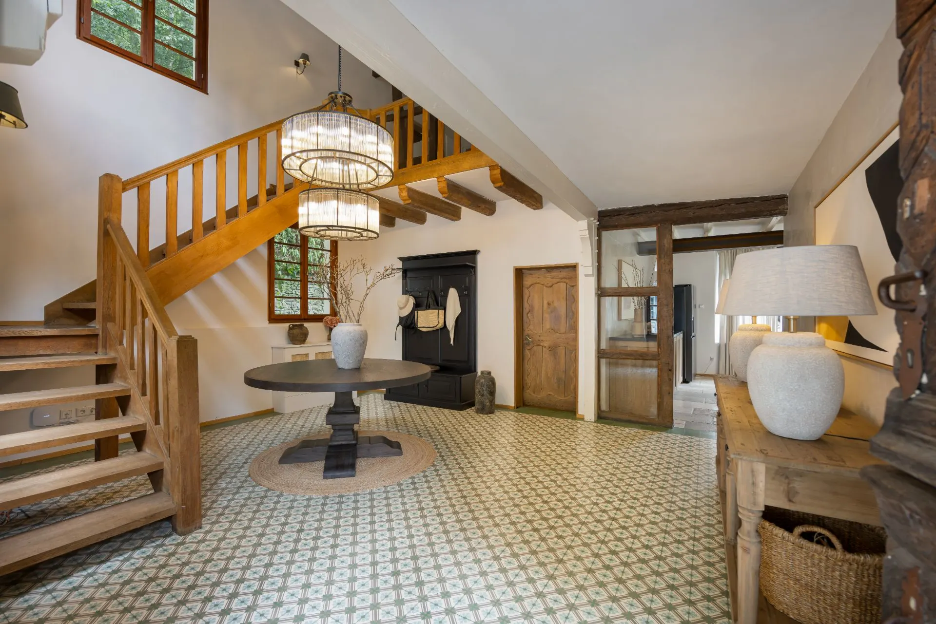 Heller Flur mit Holztreppe, rundem Tisch, Schrank und Fenster, dekorative Lampen an der Decke.