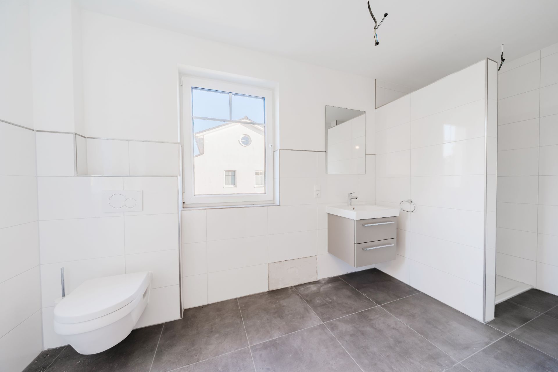 Helles, modernes Bad mit Wandtoilette, Waschbecken, Spiegel und Fenster.