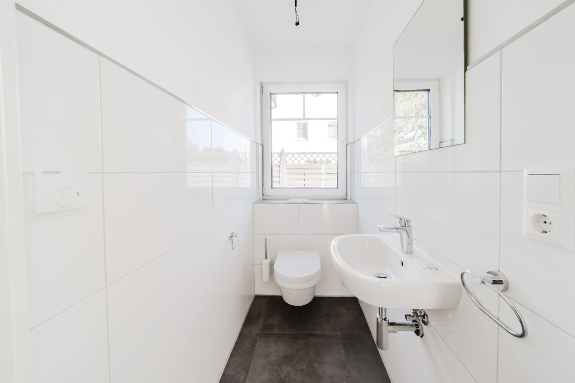 Helles, modernes Bad mit Wand-WC, Waschbecken und Fenster.