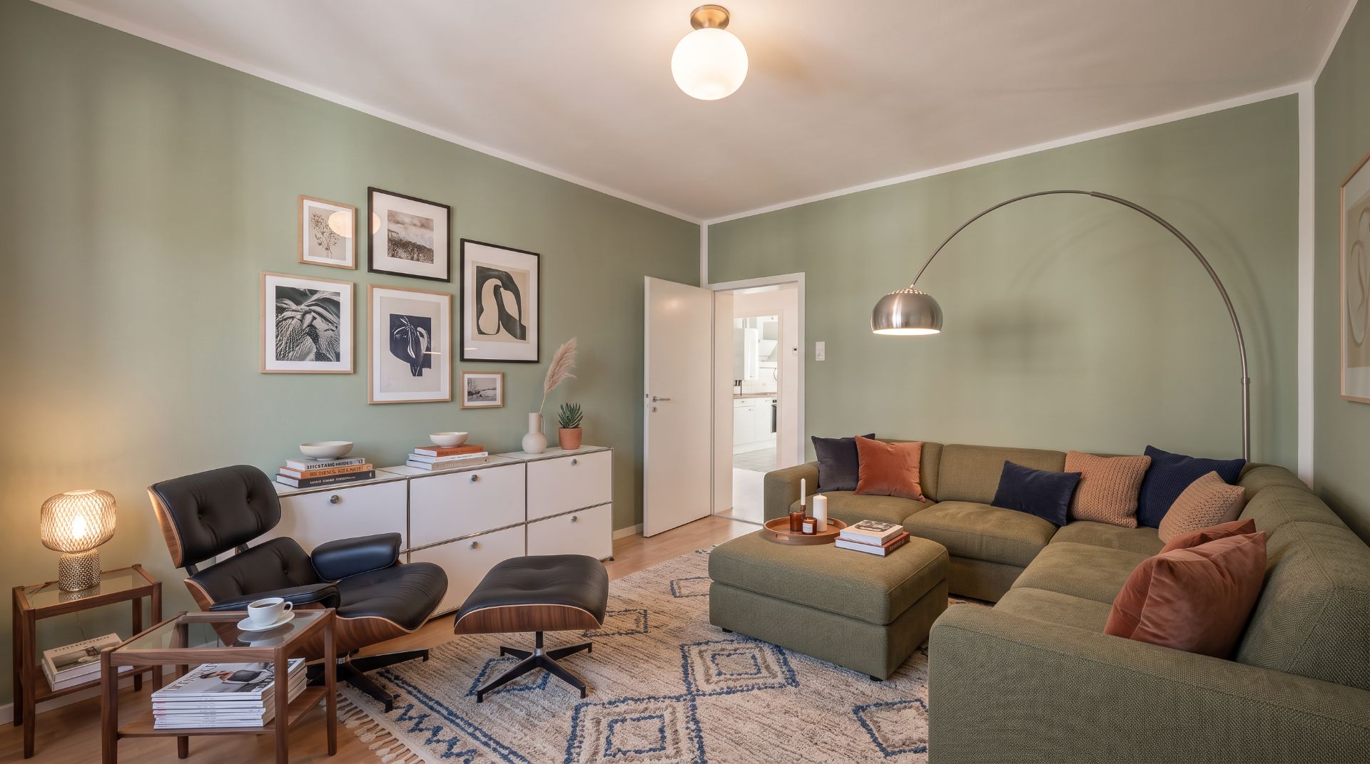 Modernes Wohnzimmer mit grüner Wand, großem Sofa, Sessel, Sideboard und Wandbildern.