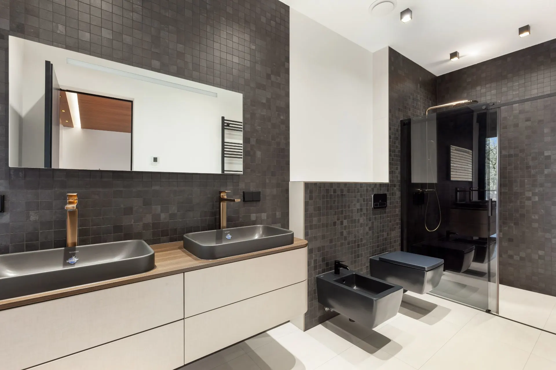 Modernes Badezimmer mit zwei Waschbecken, Dusche, WC und Bidet, dunkle Wandfliesen.