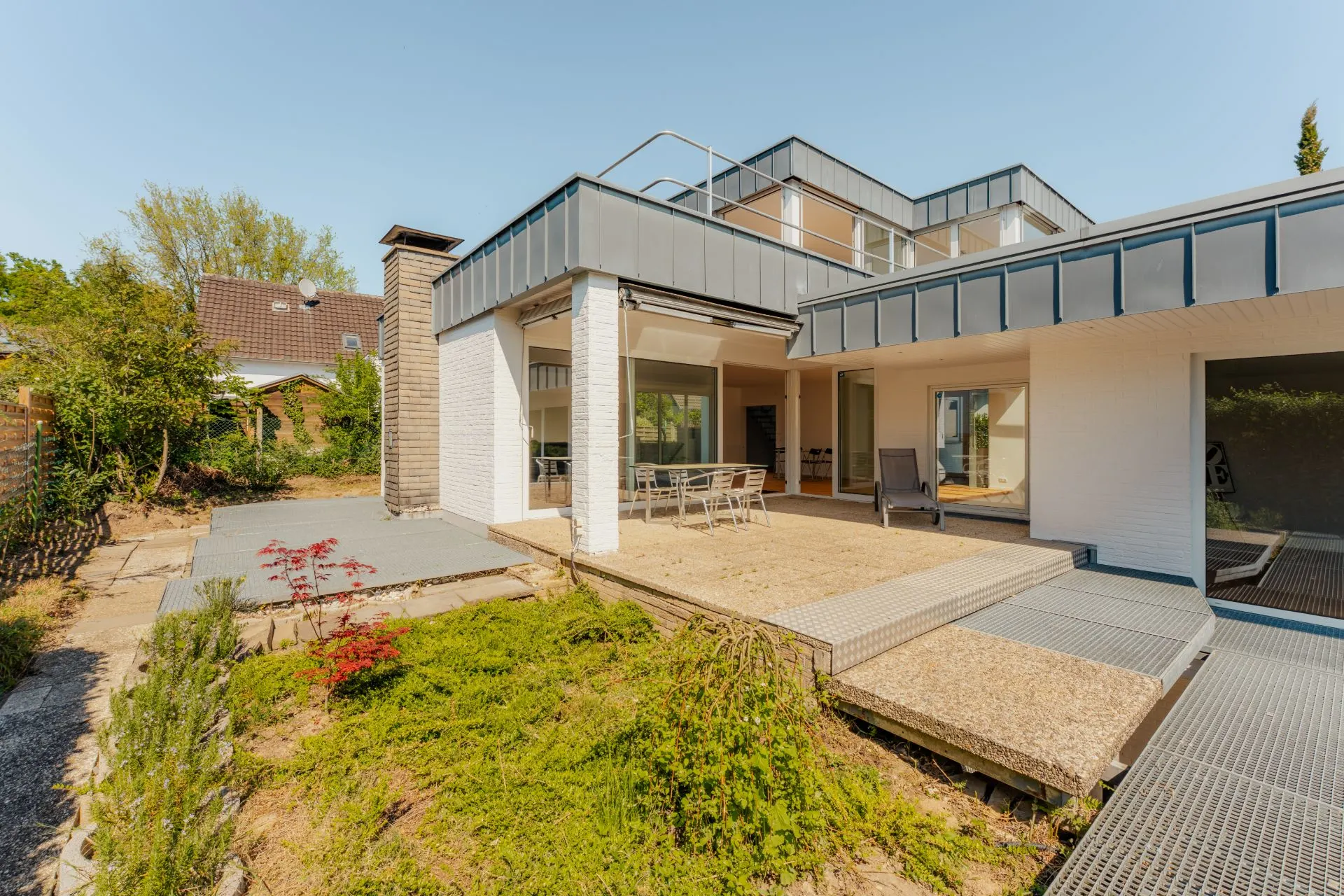 Moderne Wohnhaus-Terrasse mit Garten, Sitzbereich und großen Fenstern bei Tageslicht.