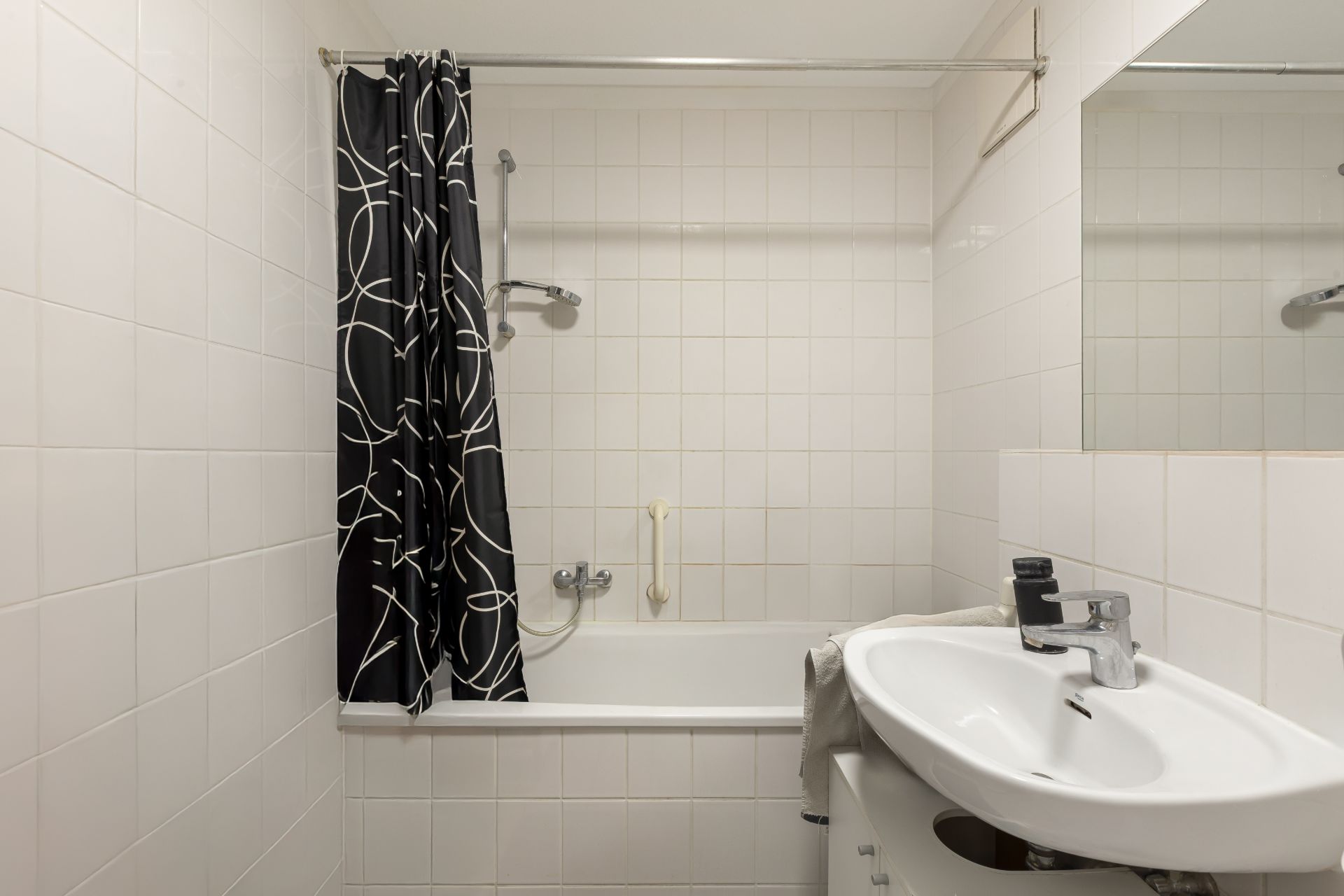 Kleines Badezimmer mit Badewanne, Duschvorhang und Waschbecken mit Spiegel.