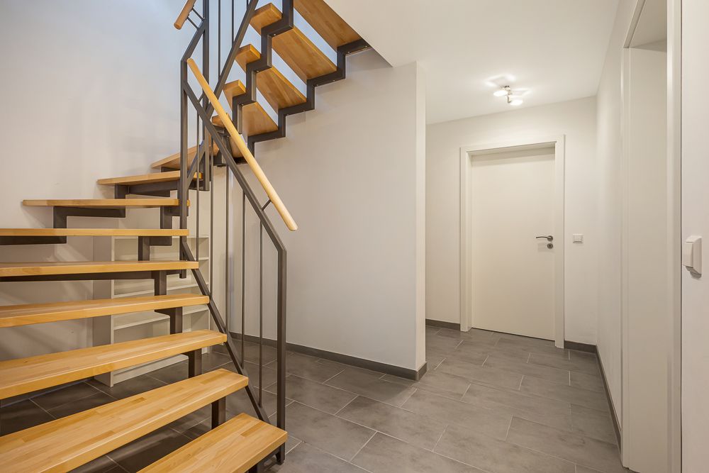 Flur mit moderner Holztreppe und grauem Fliesenboden in einem Wohnhaus.