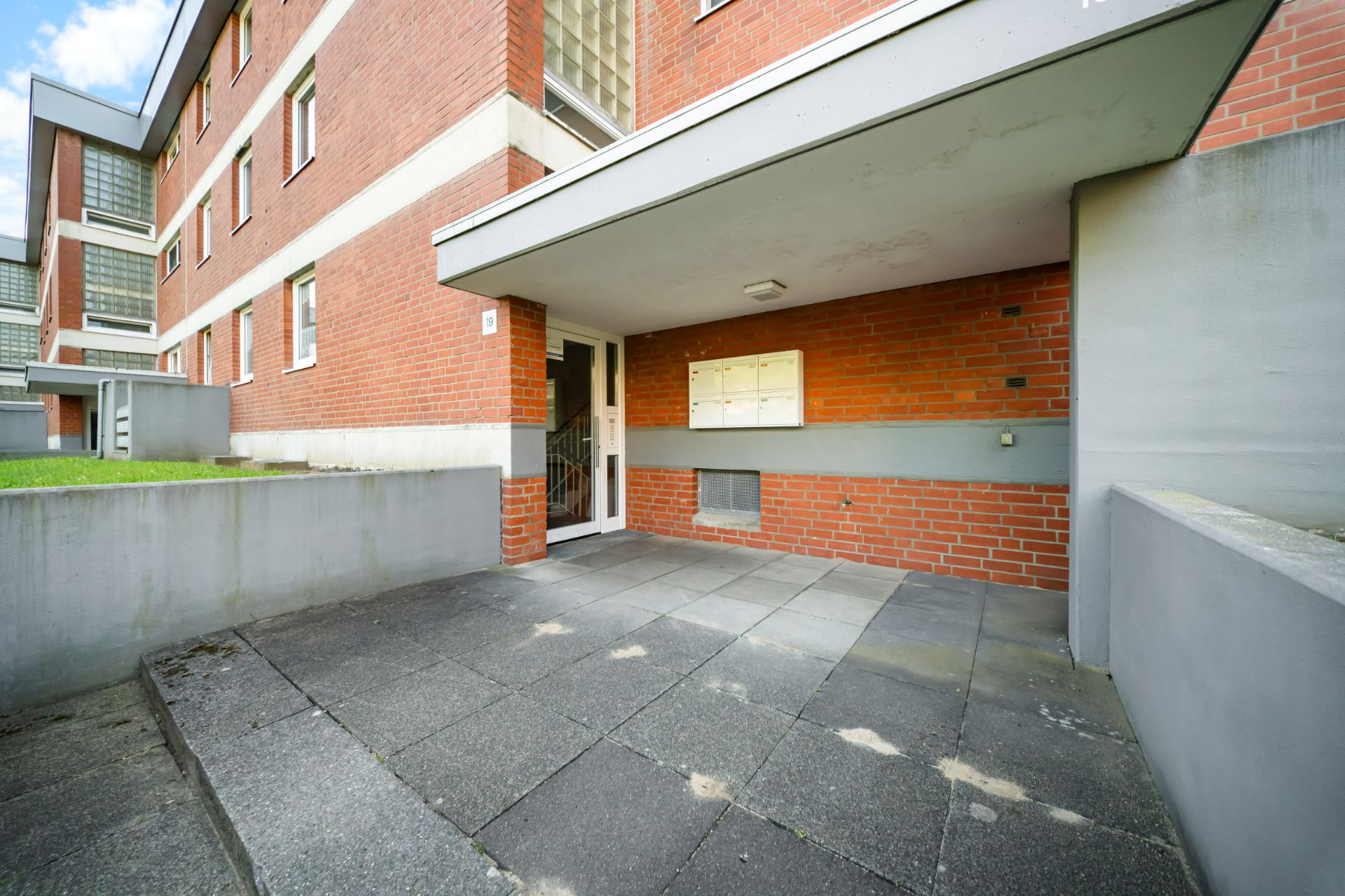 Eingang eines Mehrfamilienhauses mit roten Backsteinwänden und Briefkästen an der Wand.