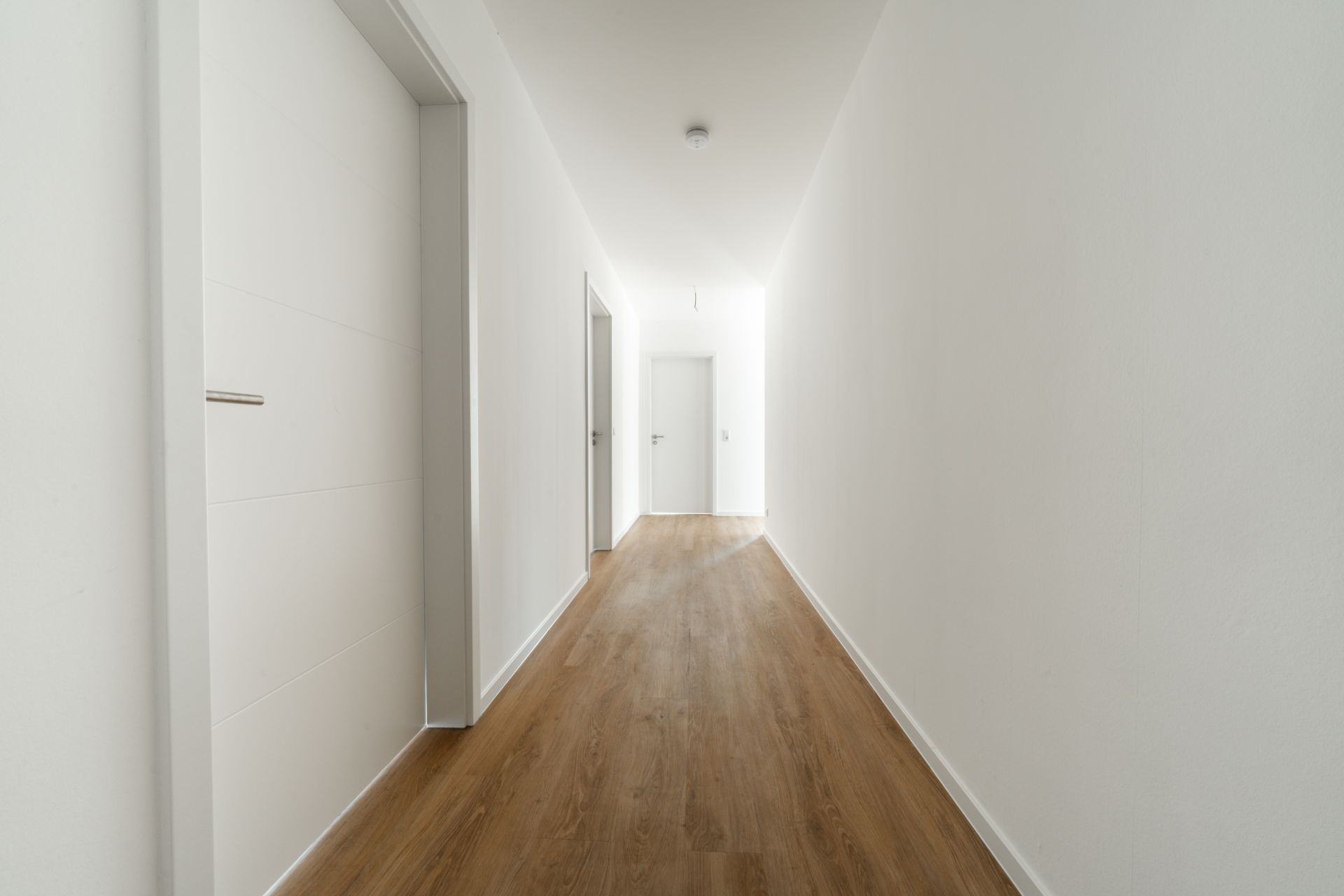 Heller Flur mit weißen Wänden und hellem Holzboden, Türen an den Seiten.