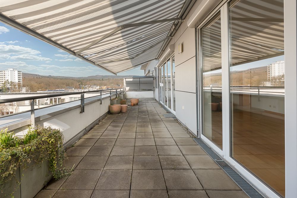 Große Dachterrasse mit Markise, Pflanzkübeln und bodentiefen Fenstern.