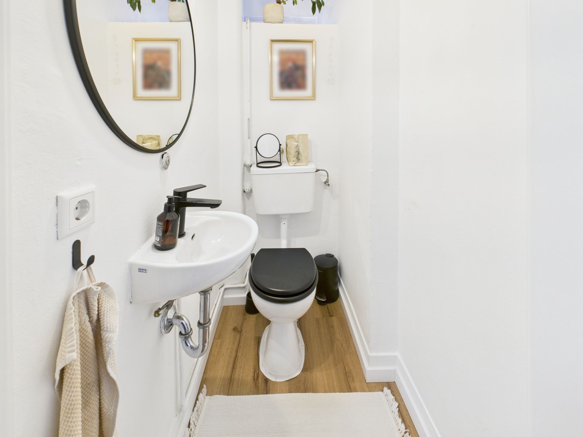Kleines Badezimmer mit Toilette, Waschbecken, Spiegel und Holzfußboden.