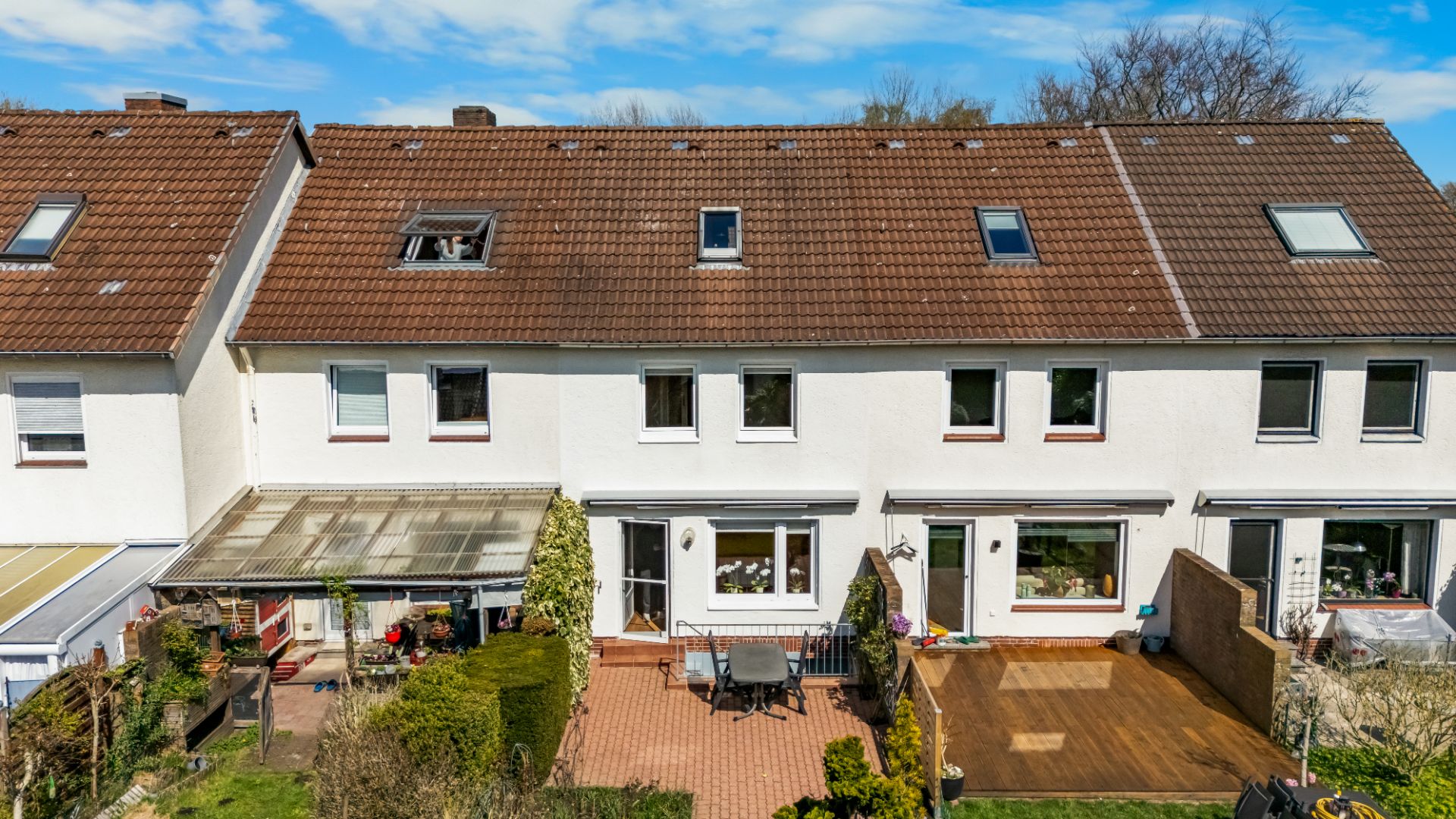 Rückseite eines weißen Reihenhauses mit Terrasse, Gartenmöbeln und bepflanztem Garten.