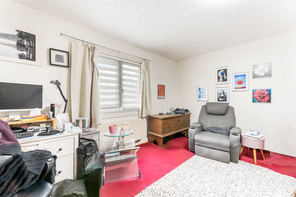 Helles Wohnzimmer mit rotem Teppich, Sessel, Schreibtisch und mehreren Bildern an der Wand.