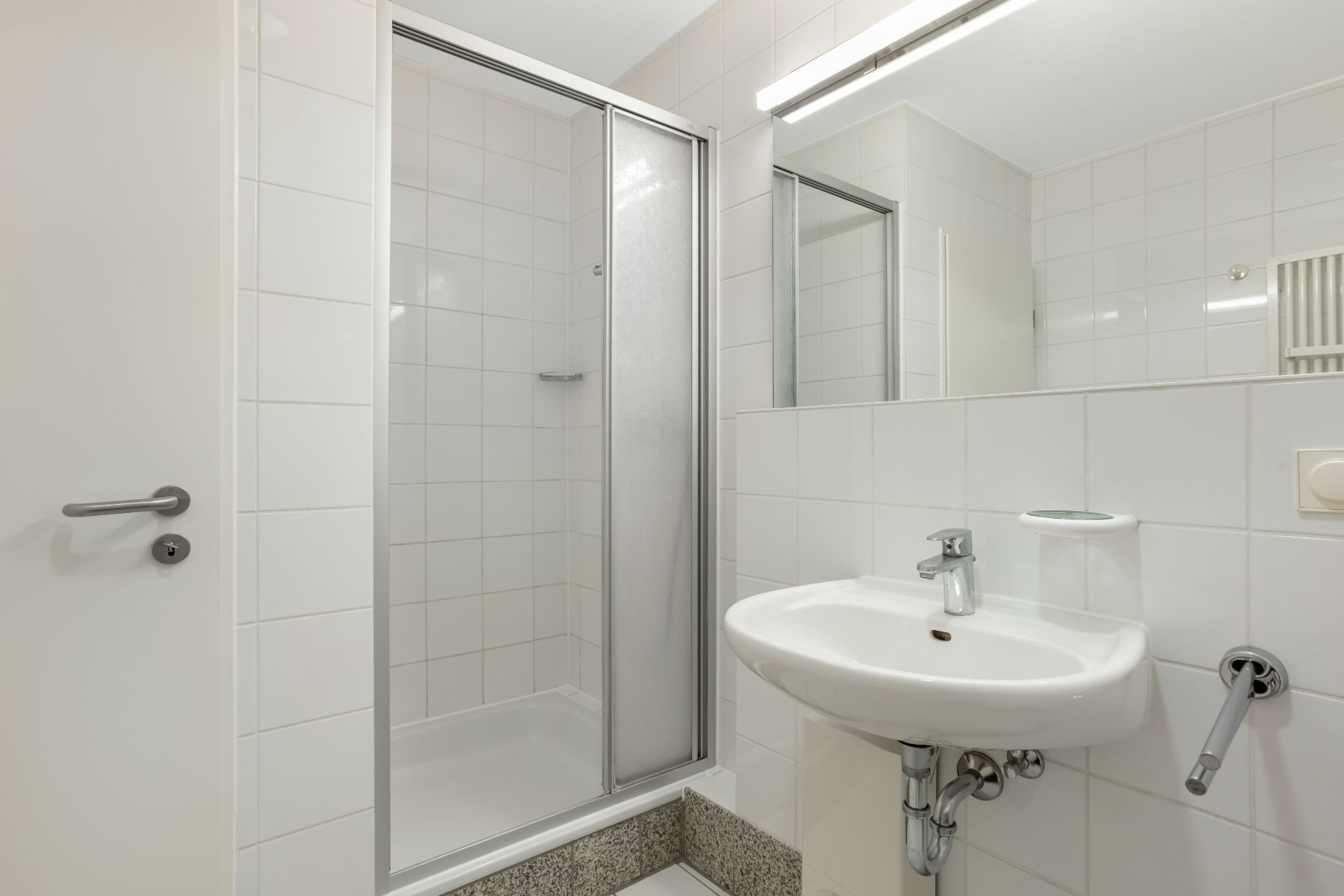 Modernes Badezimmer mit Duschkabine, Waschbecken und großem Spiegel.