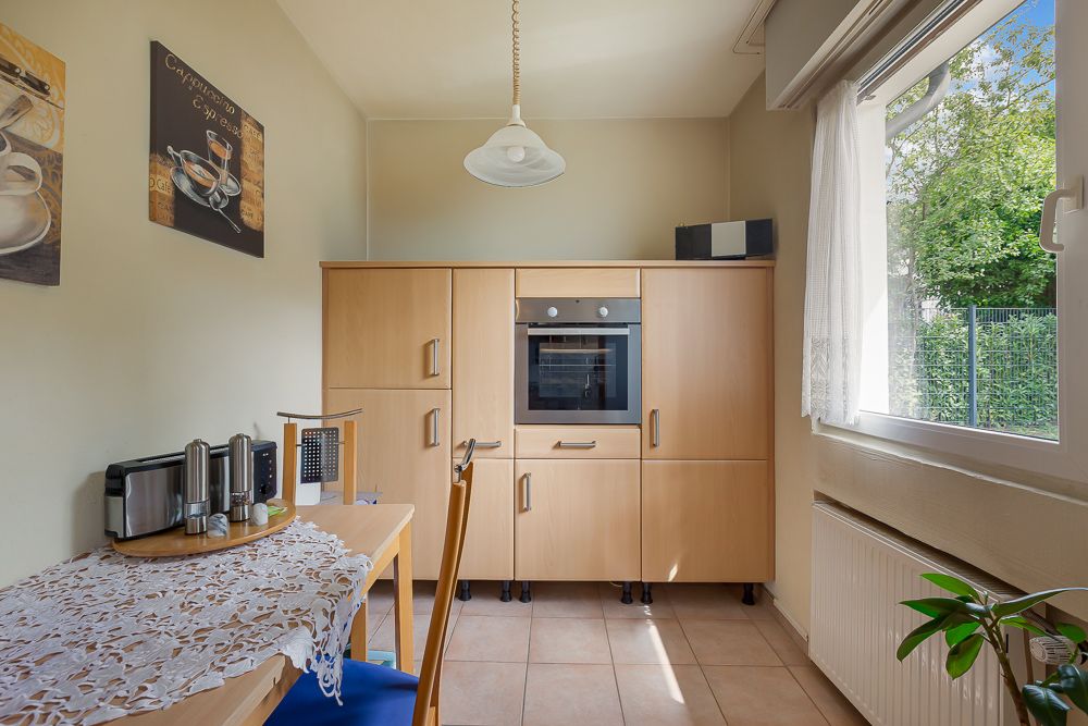 Helle Küche mit Holzschränken, Backofen, Esstisch, Fenster und Wanddekoration.