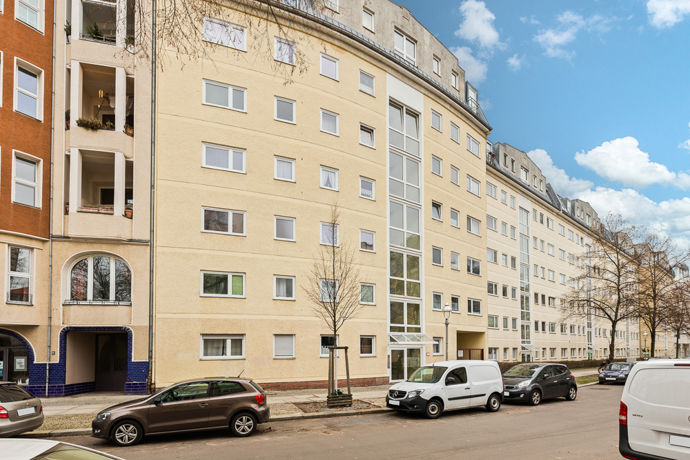 Mehrstöckiges Wohnhaus mit gelber Fassade, vielen Fenstern und parkenden Autos auf der Straße.