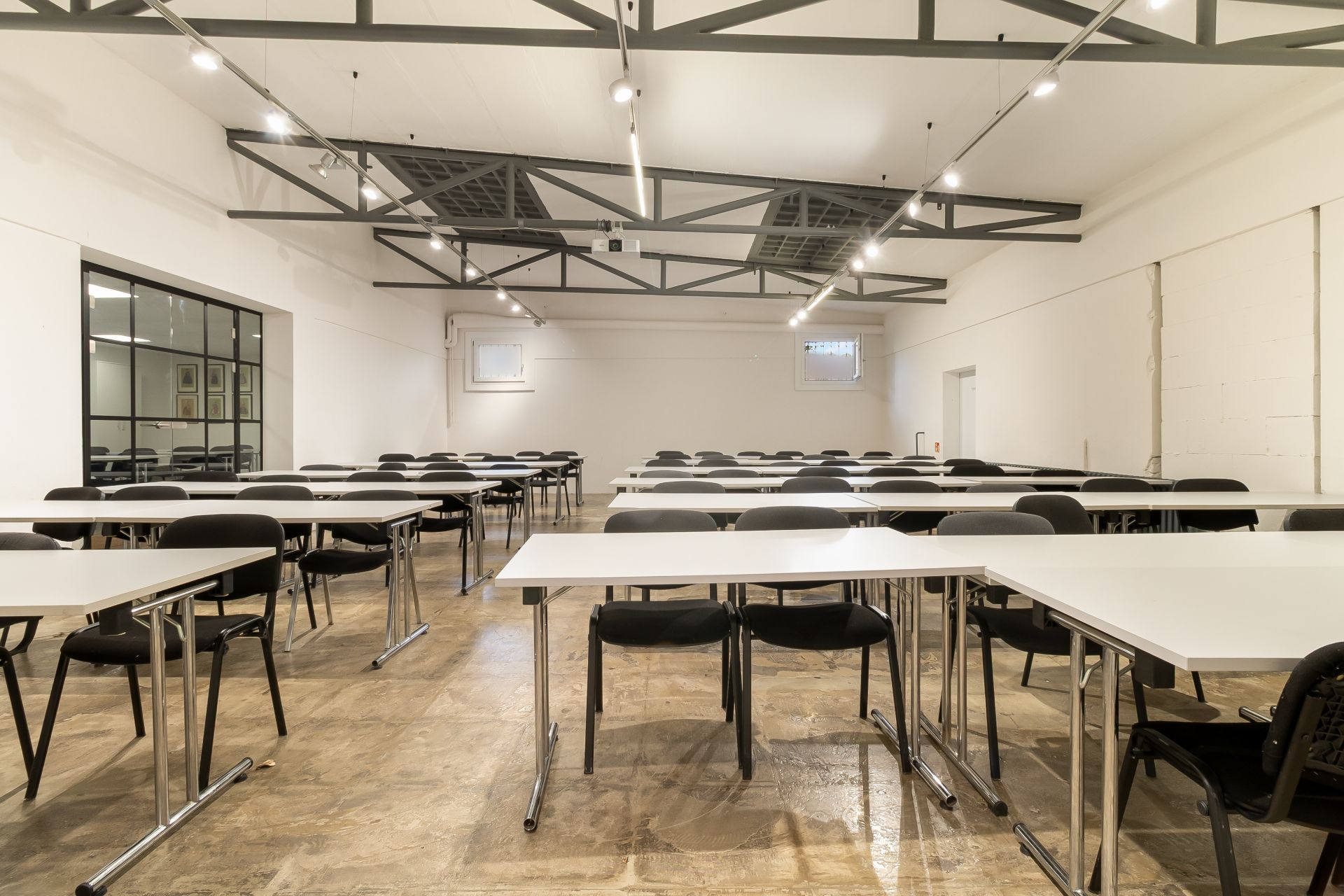 Großer heller Raum mit vielen Tischen und Stühlen, sichtbare Decke mit Metallträgern.