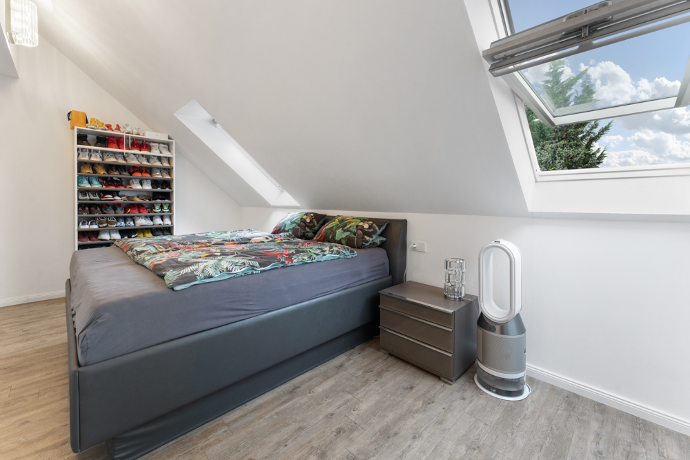 Schlafzimmer mit Doppelbett, Schuhregal, Nachttisch und großem Dachfenster.